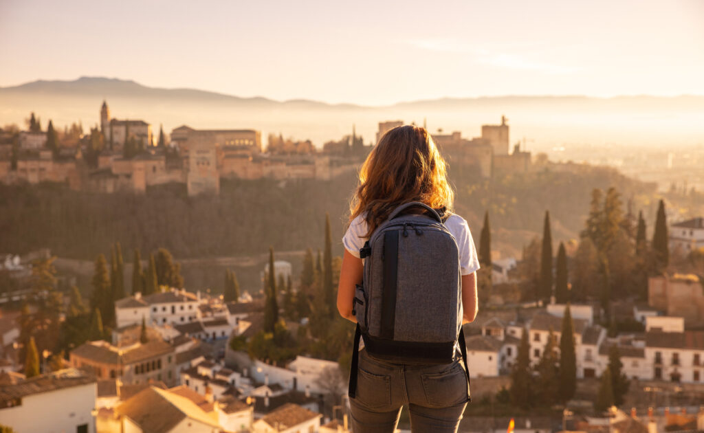 A young woman with a backpack looks over a city, illustrating the post-pandemic shift in the travel industry to experienced-based travel.